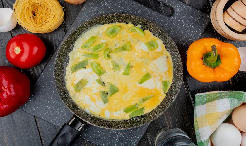 Sartén con tortilla de verduras sobre encimera de cocina con ingredientes frescos alrededor