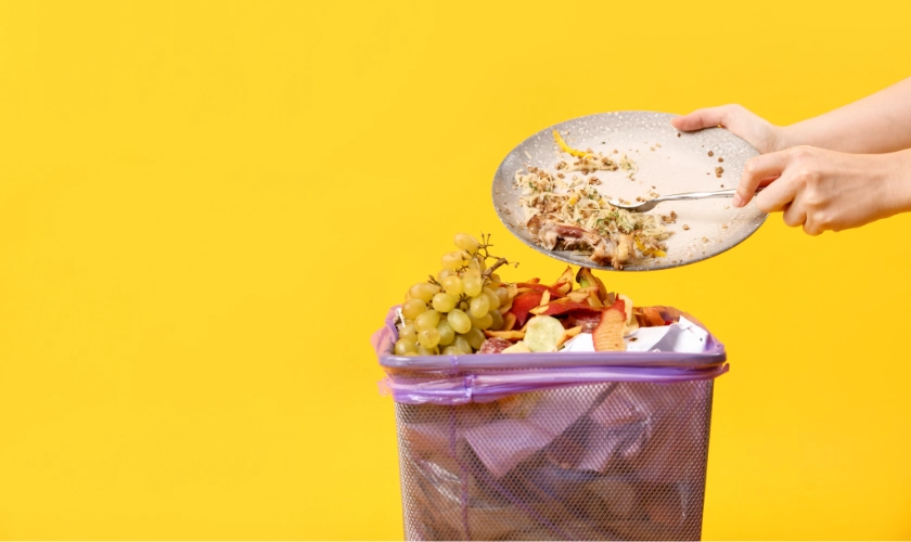 Persona tirando comida a la papelera generando desperdicio alimentario
