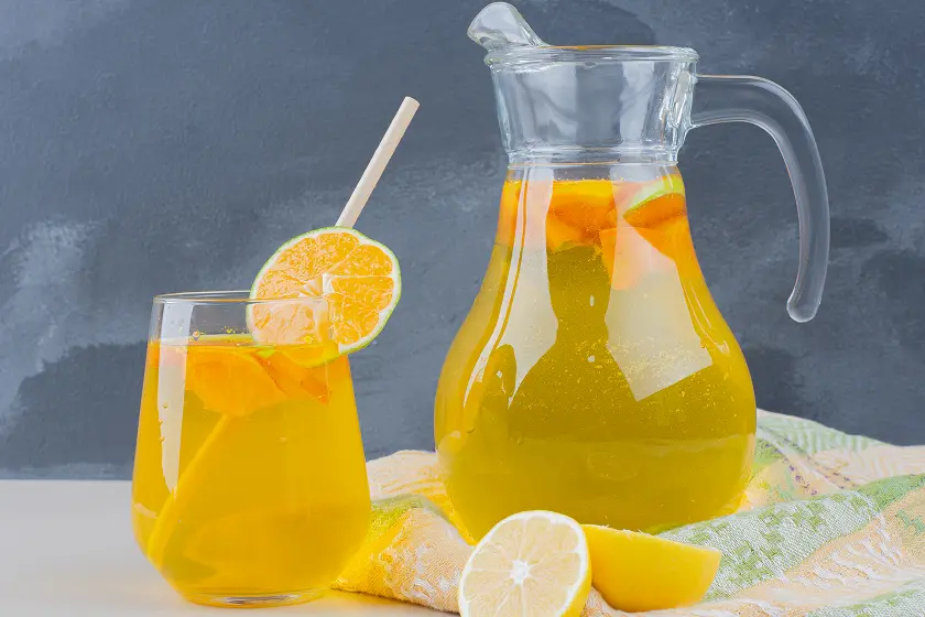 Jarra de Agua de Valencia con naranjas cortadas, hielo y copas de cava sobre mesa con fondo mediterráneo
